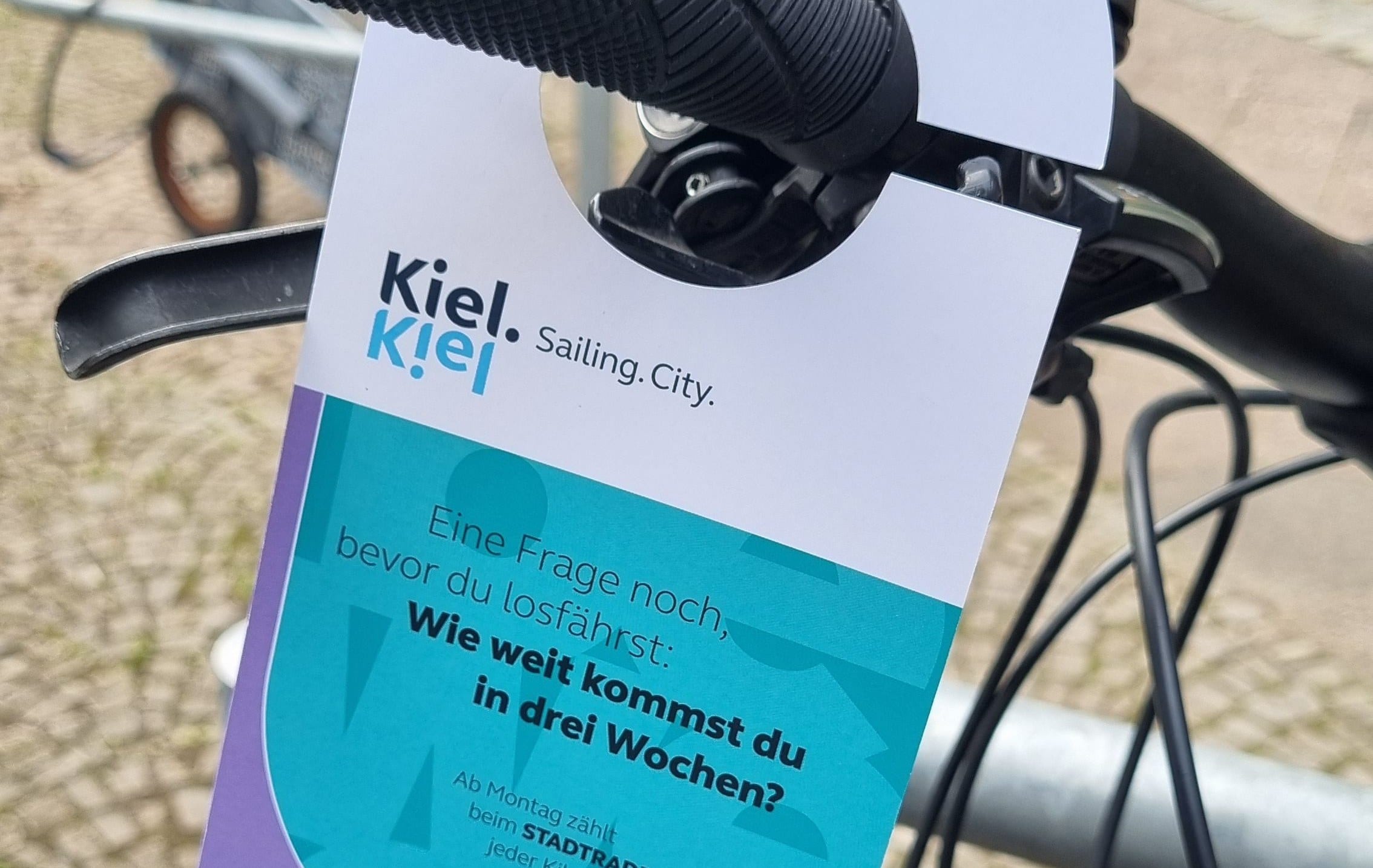 Türanhänger der Stadtradeln-Kampagne an einem Fahrradlenker mit der Frage: Wie weit kommst du in drei Wochen?